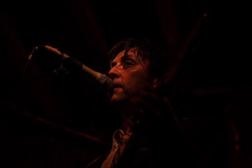 Ben at the microphone bathed in deep red stage light during a moody live performance.